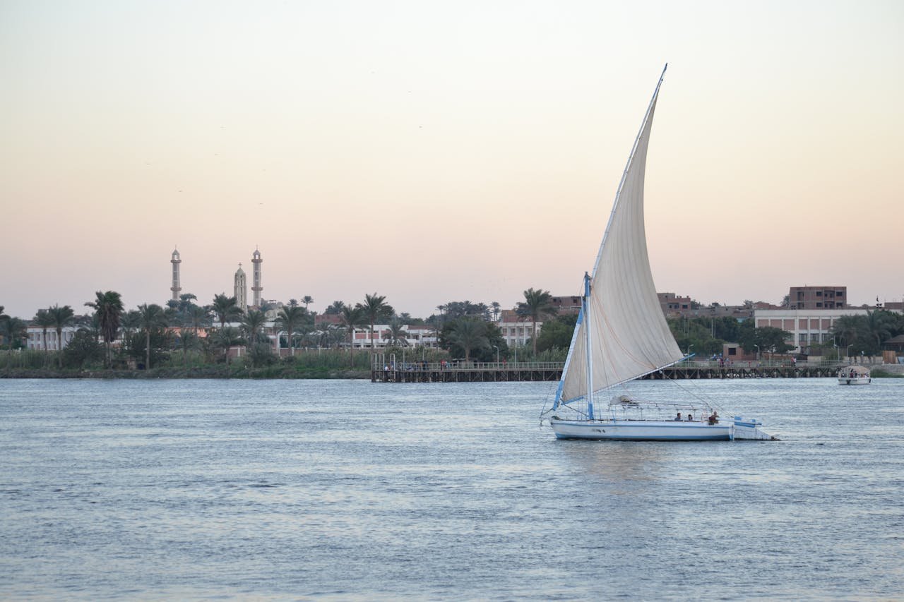 A serene view of a sailboat cruising the Nile River with a backdrop of Cairo landmarks at sunset.